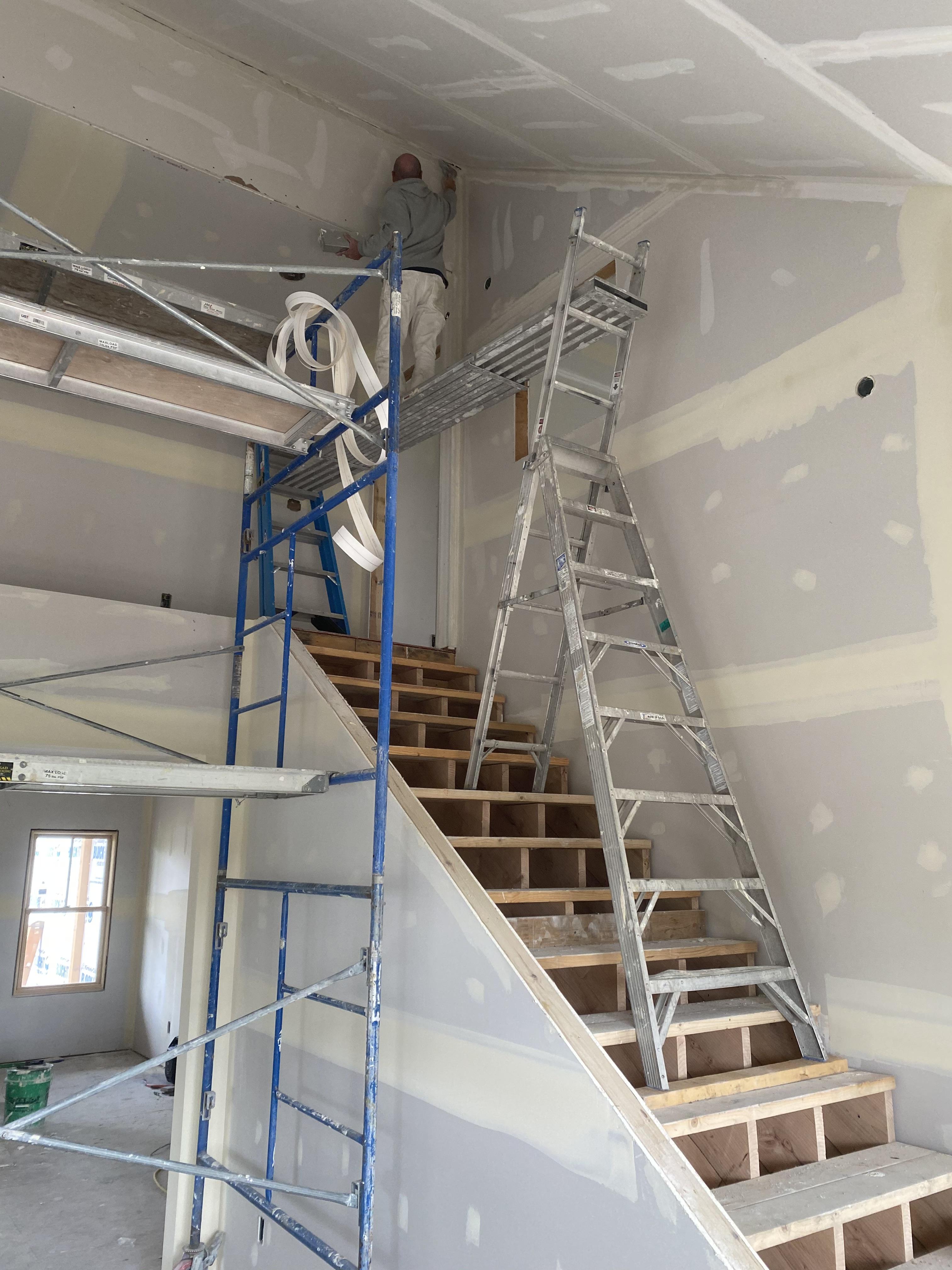 Worker reaching a distant corner on a staircase with scaffolding.